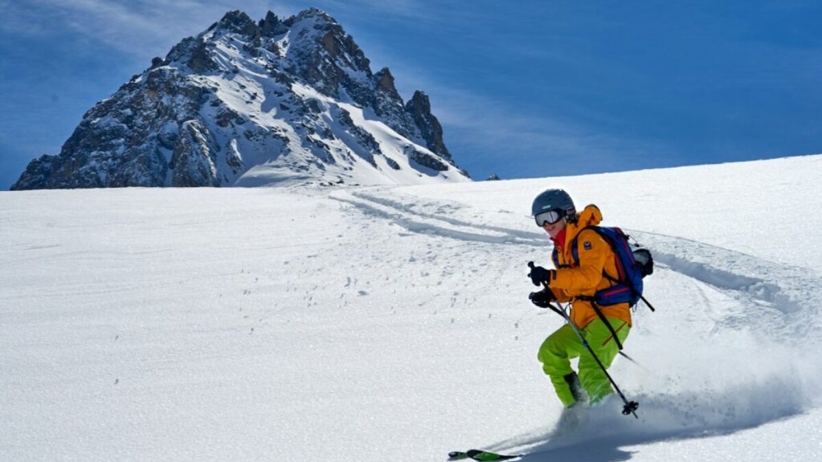 man in orange jacket and black pants riding ski blades on snow covered mountain during daytime