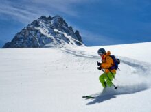 man in orange jacket and black pants riding ski blades on snow covered mountain during daytime