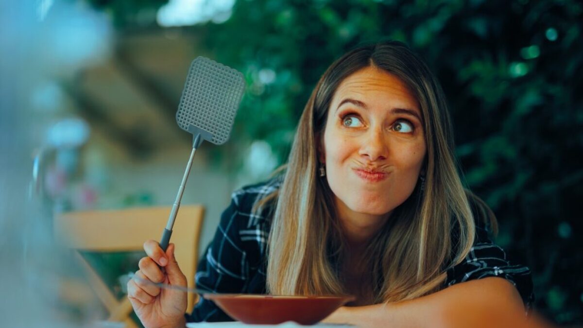 Žena sedící u stolu se snaží plácačkou zabít mouchu