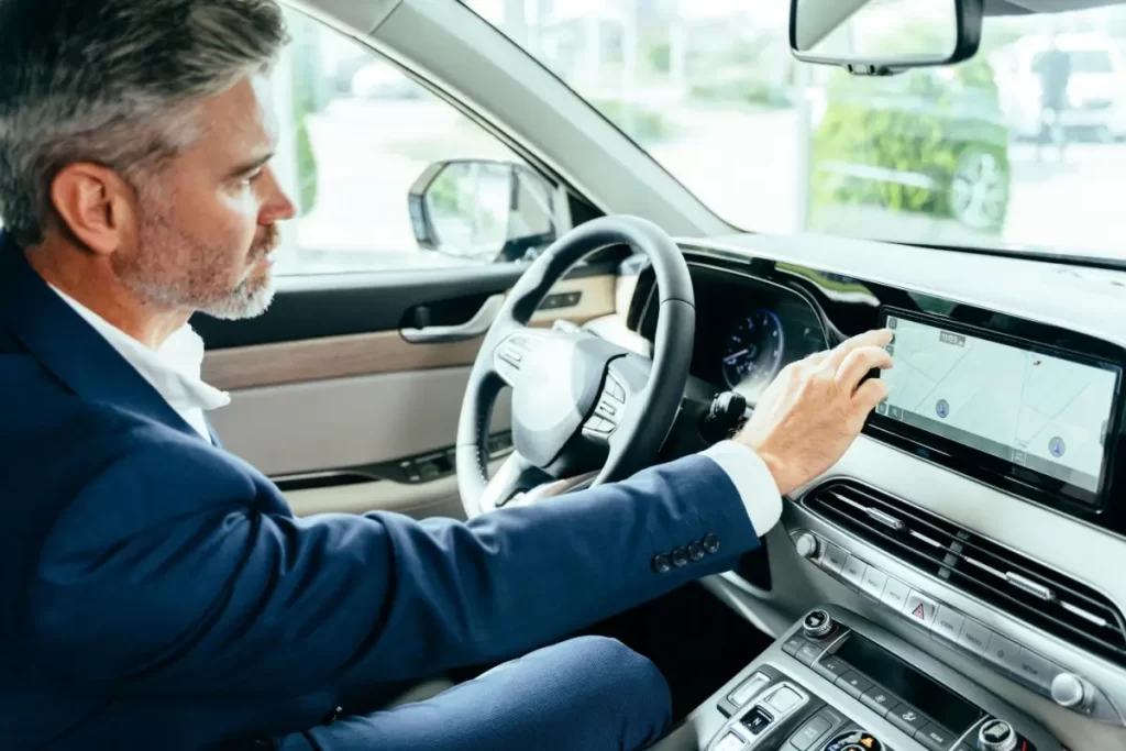 Shutterstock_2234470705 - SportDeník Muž středního věku sedí v autě a nastavuje navigaci na palubním displeji.