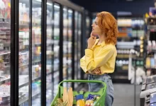 Žena si zkoumavě prohlíží regály se zbožím v supermarketu