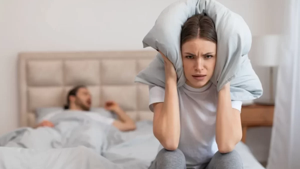 Žena zacpávající si uši polštářem kvůli partnerově chrápání