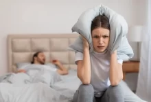 Žena zacpávající si uši polštářem kvůli partnerově chrápání