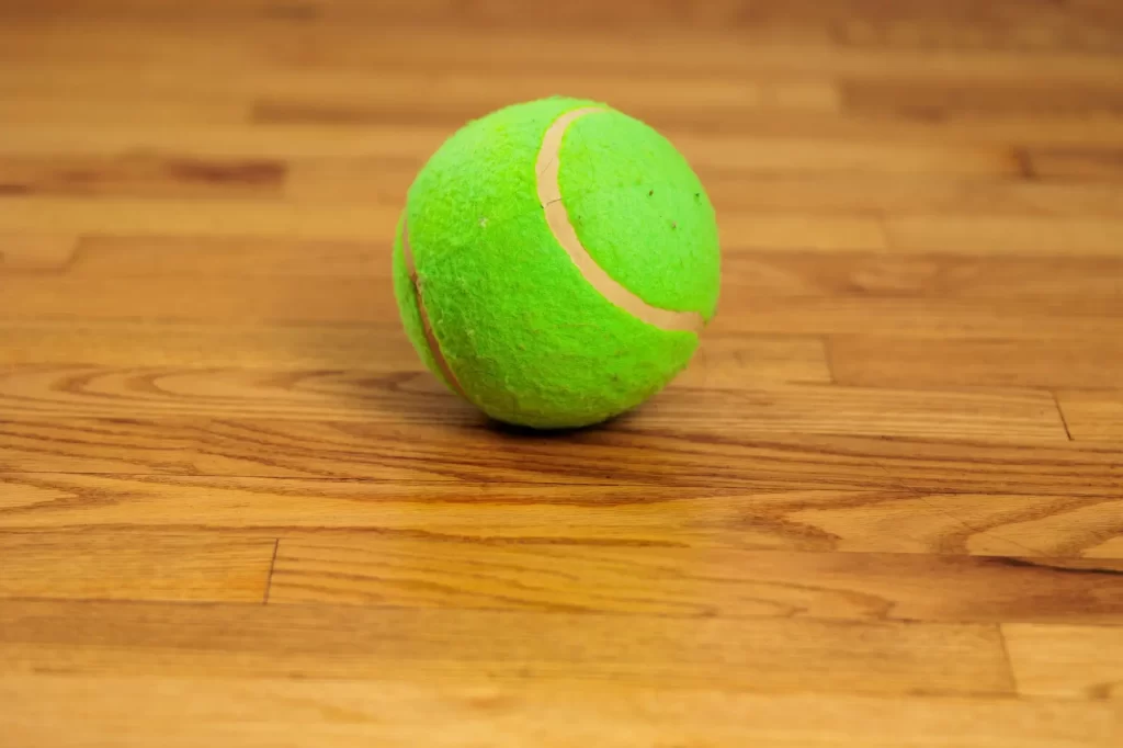 Shutterstock_2455674789 - SportDeník Zelený tenisák na dřevěné podlaze