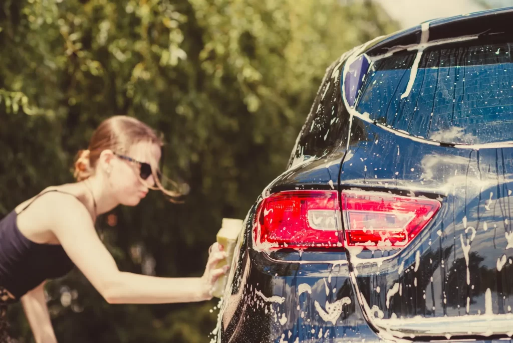 mytí před - SportDeník žena ve slunečních brýlích myje auto houbičkou