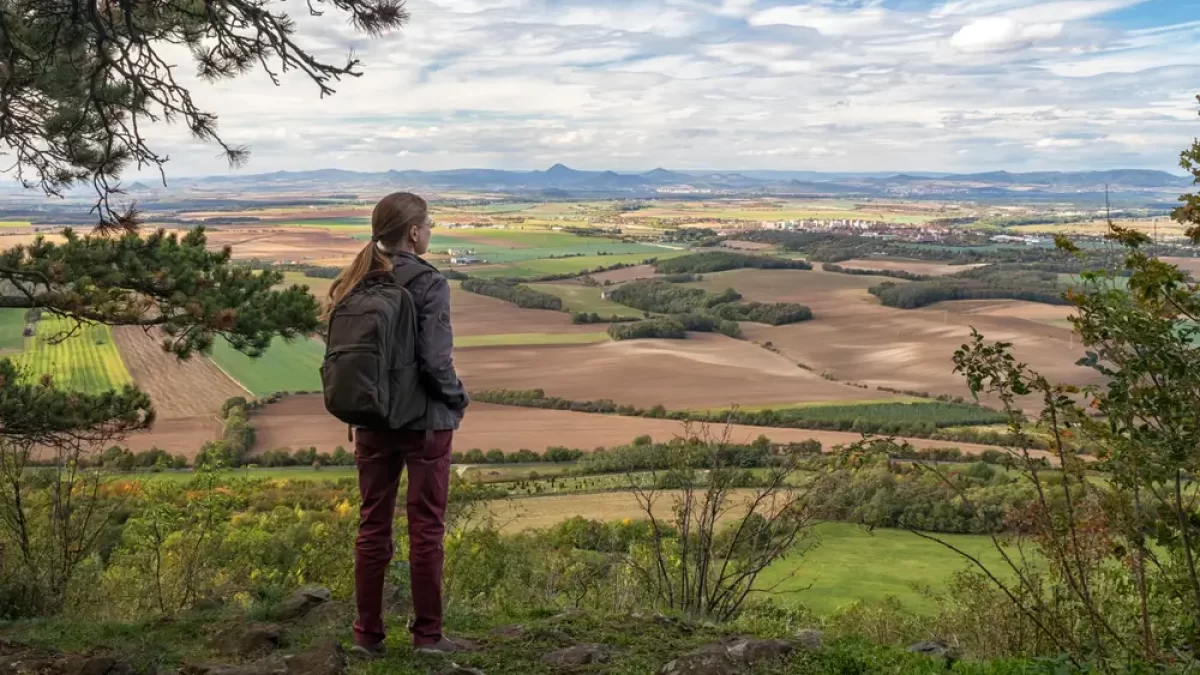 Výhled na krajinu z hory Říp v Česku. Na fotografii se nachází žena s batohem.
