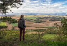 Výhled na krajinu z hory Říp v Česku. Na fotografii se nachází žena s batohem.