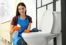 Mladá žena čistí záchodové prkénko. Usmívá se.
