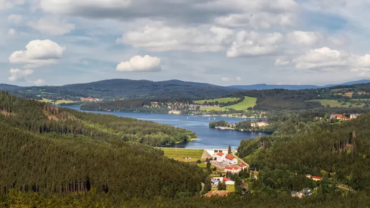 Vodní nádrž Lipno z leteckého pohledu. V okolí se nachází zalesněná krajina.