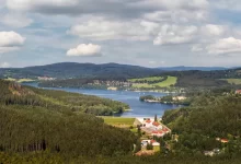 Vodní nádrž Lipno z leteckého pohledu. V okolí se nachází zalesněná krajina.
