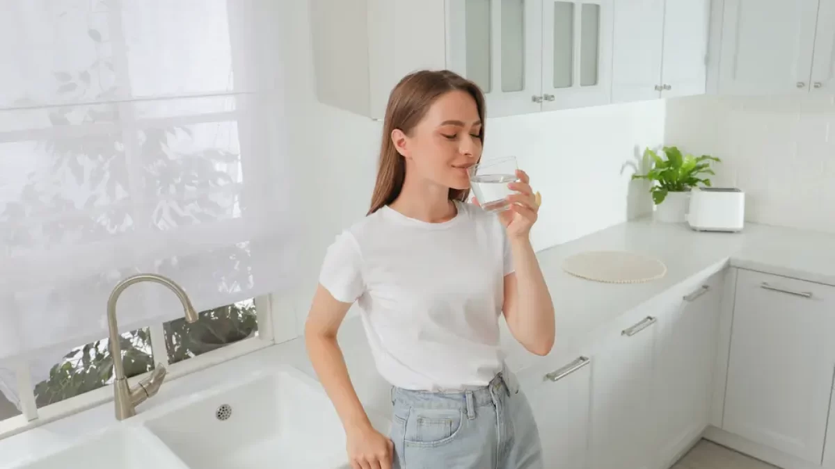 Žena pije vodu u prázdného bílého dřezu.