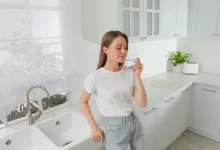 Žena pije vodu u prázdného bílého dřezu.