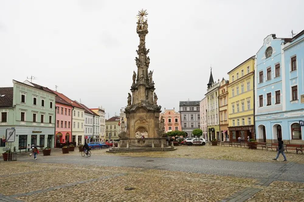 shutterstock_2246355319 - SportDeník Barokní sloup se sousoším Nejsvětější Trojice na náměstí v Jindřichově Hradci. Po jeho kamenné dlažbě chodí lidé.