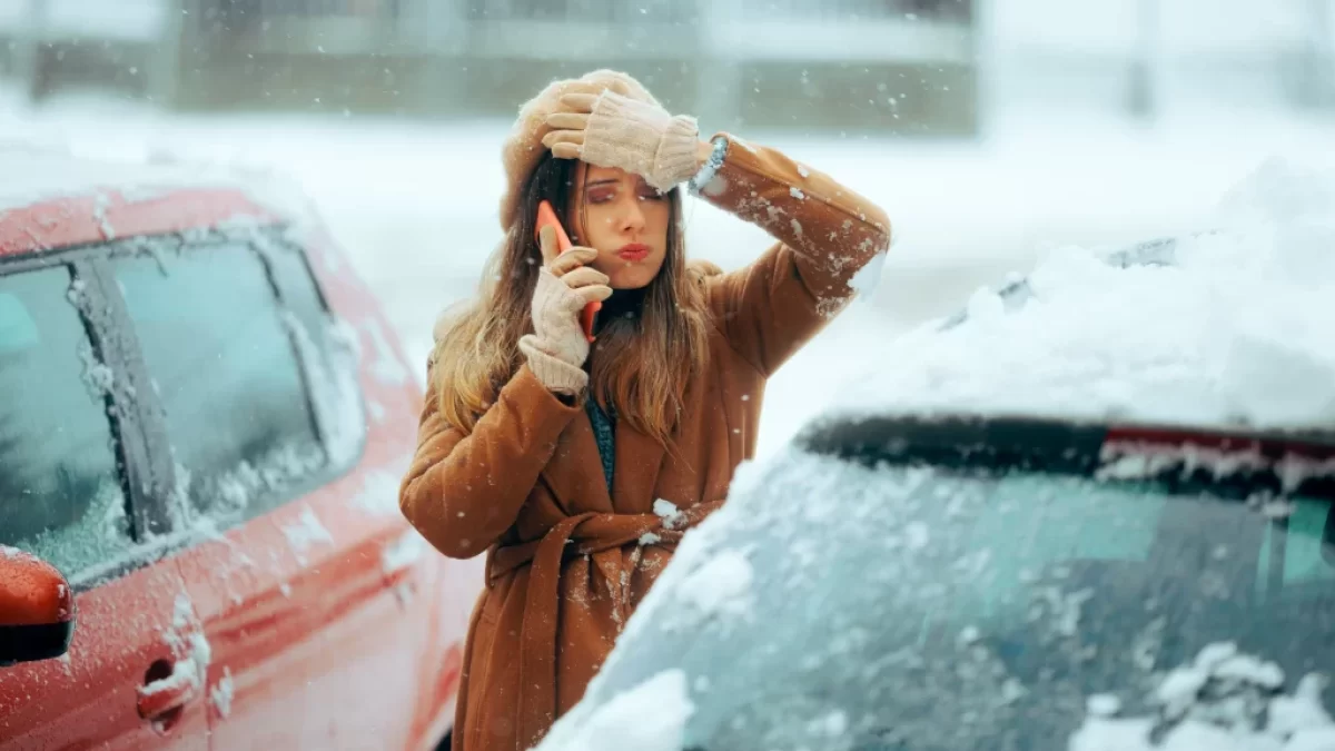 Žena si neví rady vedle auta v zimě a telefonuje.