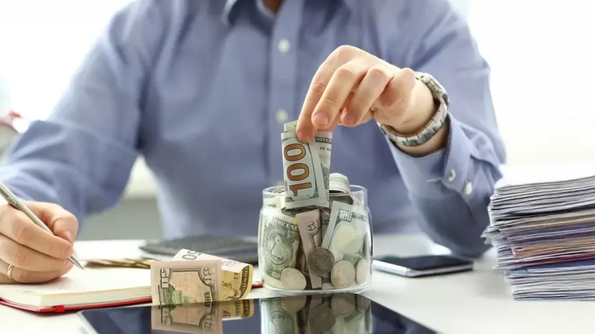 Muž v košili odkládá bankovku do kasičky.
