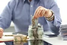 Muž v košili odkládá bankovku do kasičky.