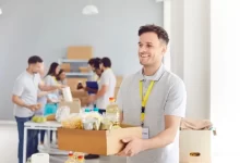 Pracovník charitativní organizace drží v ruce bednu s věcmi. Za ním stojí jeho kolegové.