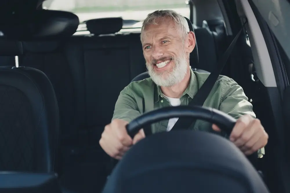 - SportDeník Starší muž řídí auto.