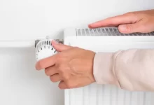 žena reguluje teplotu na radiátoru a rukou kontroluje jeho teplotu