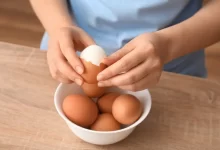 Žena loupe vejce. Na záběru jsou pouze její ruce.
