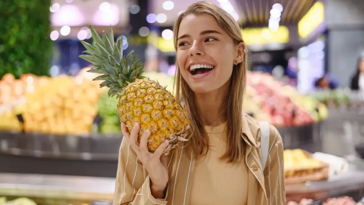 Mladá žena se usmívá. V ruce drží ananas.