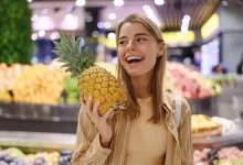 Mladá žena se usmívá. V ruce drží ananas.