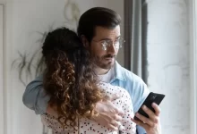 Muž drží ženu kolem ramen a přitom se dívá do mobilního telefonu
