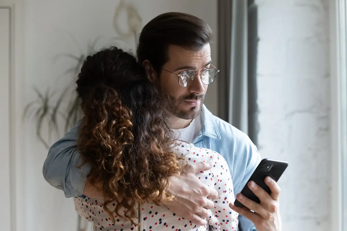 Muž drží ženu kolem ramen a přitom se dívá do mobilního telefonu