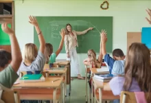 Třída s hlásícími se žáky a paní učitelkou před tabulí