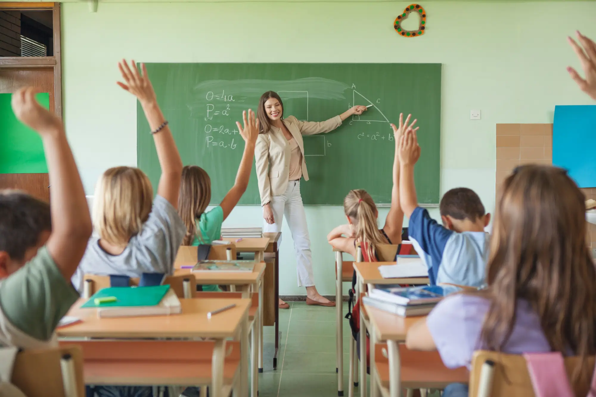 Třída s hlásícími se žáky a paní učitelkou před tabulí