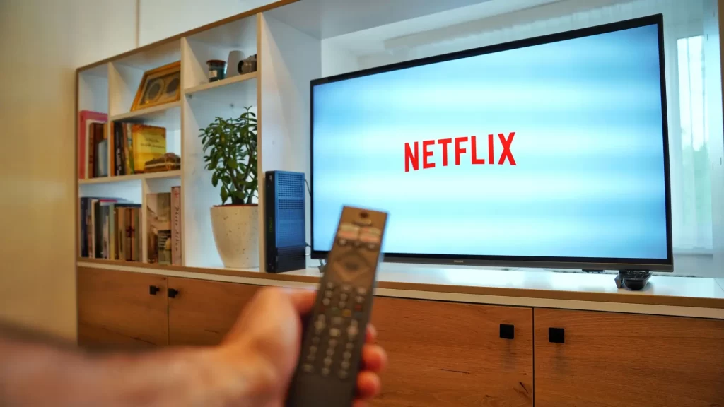 Shutterstock_2449695225 - SportDeník Ruka držící televizní ovladač mířící na televizi s nápisem Netflix na obrazovce