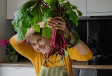 Mladá rozesmátá žena drží nad hlavou svazek červené řepy
