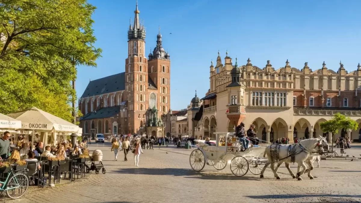 Pohled na centrum polského města Krakov s typickým kočárem taženým koňmi a plnou zahrádkou před jednou z restaurací