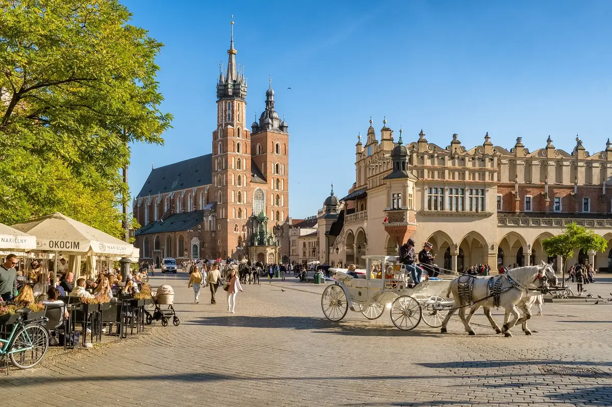 Pohled na centrum polského města Krakov s typickým kočárem taženým koňmi a plnou zahrádkou před jednou z restaurací
