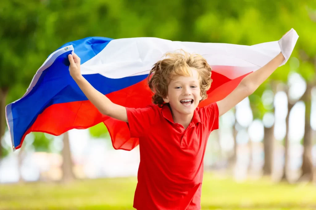 Malý kluk běžící parkem a držící českou vlajku