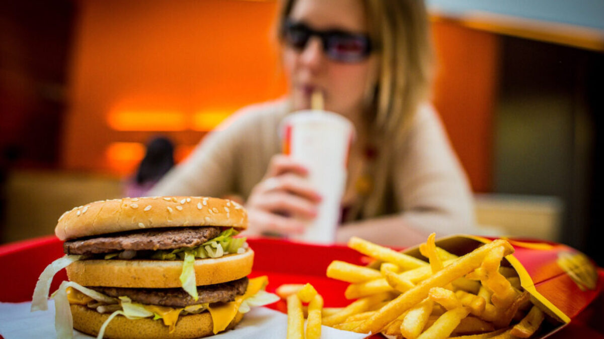 Hamburger s hranolkami a sedící ženou v pozadí