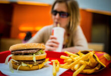 Hamburger s hranolkami a sedící ženou v pozadí