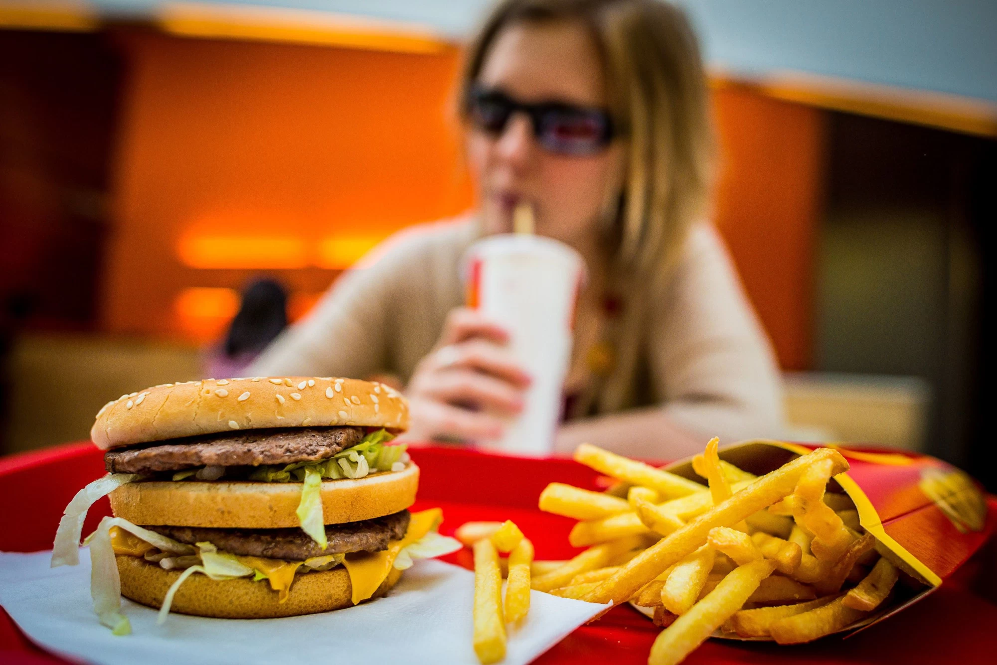 Hamburger s hranolkami a sedící ženou v pozadí