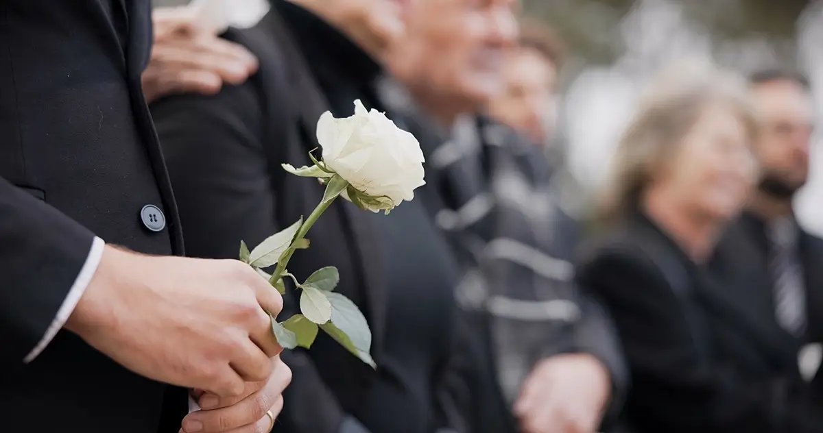 Smuteční hosté stojící v řadě na pohřbu, v popředí ruce s bílou růží
