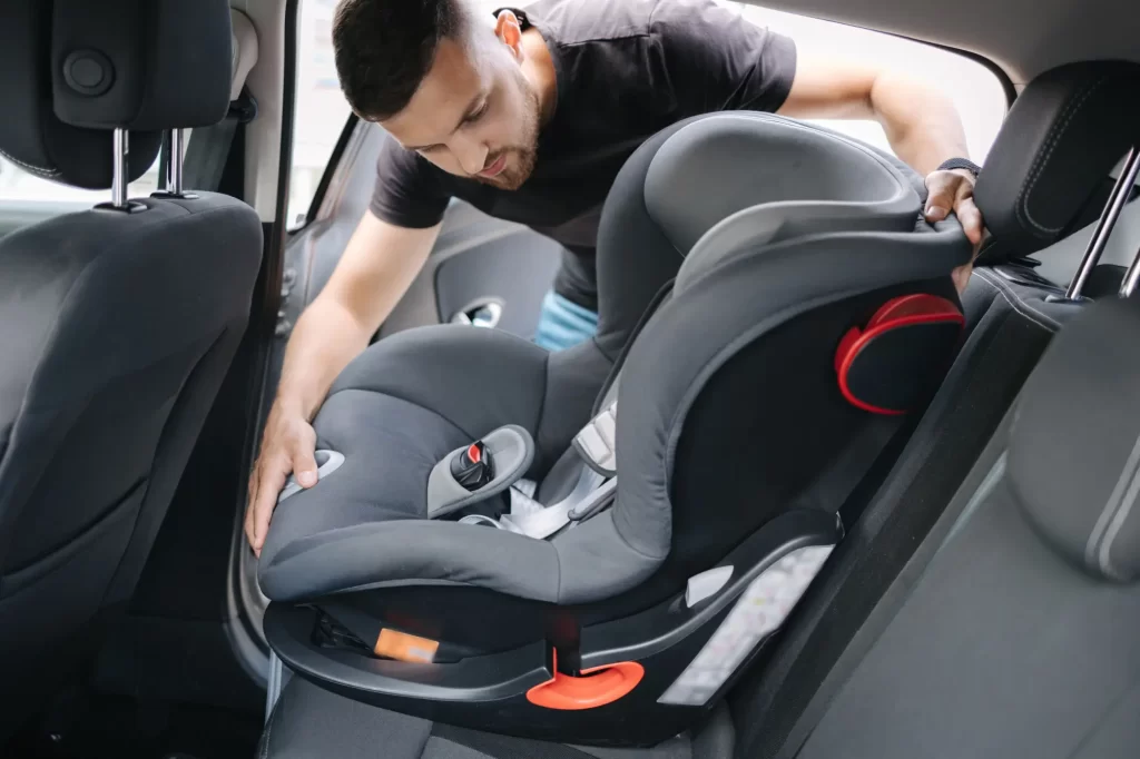 Mladý muž instalující dětskou autosedačku do vozu