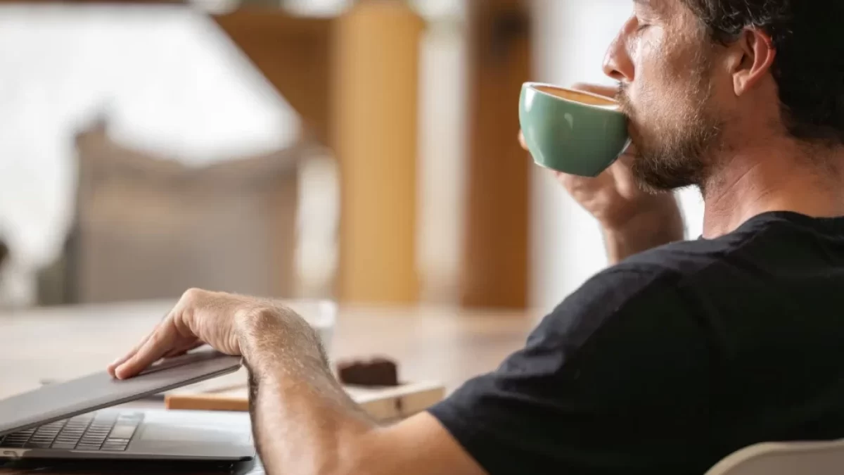 Mladý muž zavírající notebook a popíjející kávu