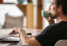 Mladý muž zavírající notebook a popíjející kávu