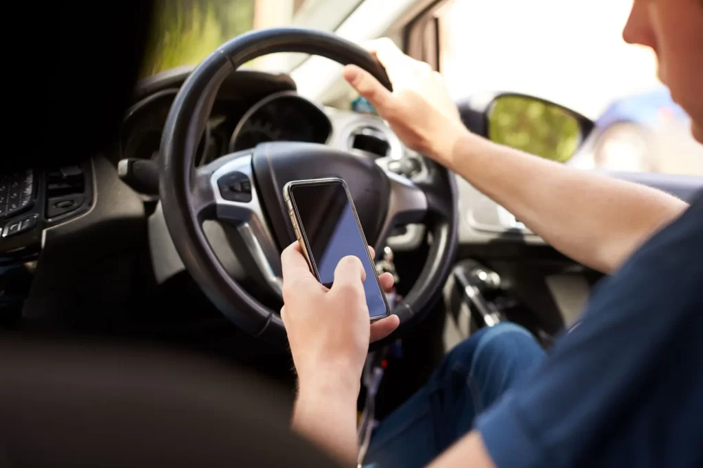 Muž koukající do mobilu během řízení auta