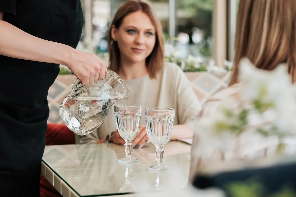 Voda 3 - SportDeník Restauratér nalévá dvěma mladým ženám vodu do sklenic