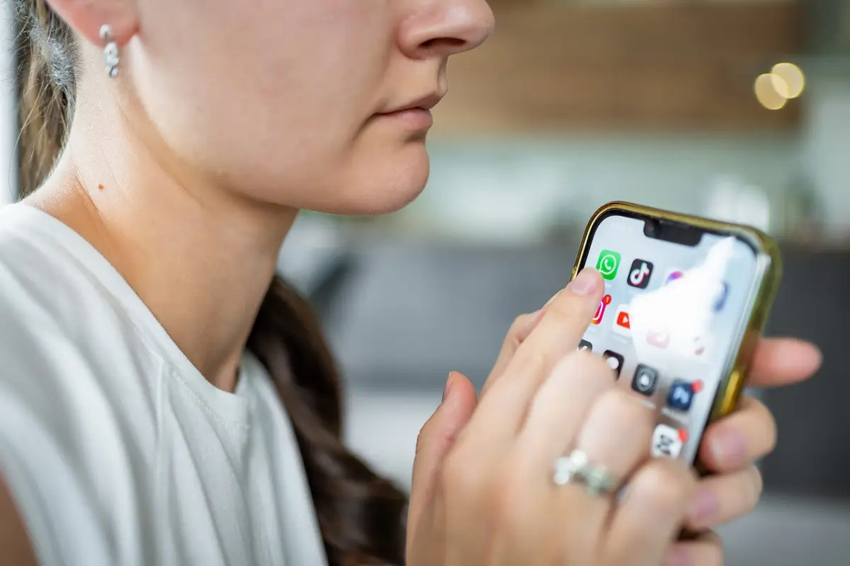 Whatsapp 3 - SportDeník Mladá žena drží v ruce telefon a chystá se kliknout na ikonku platformy WhatsApp