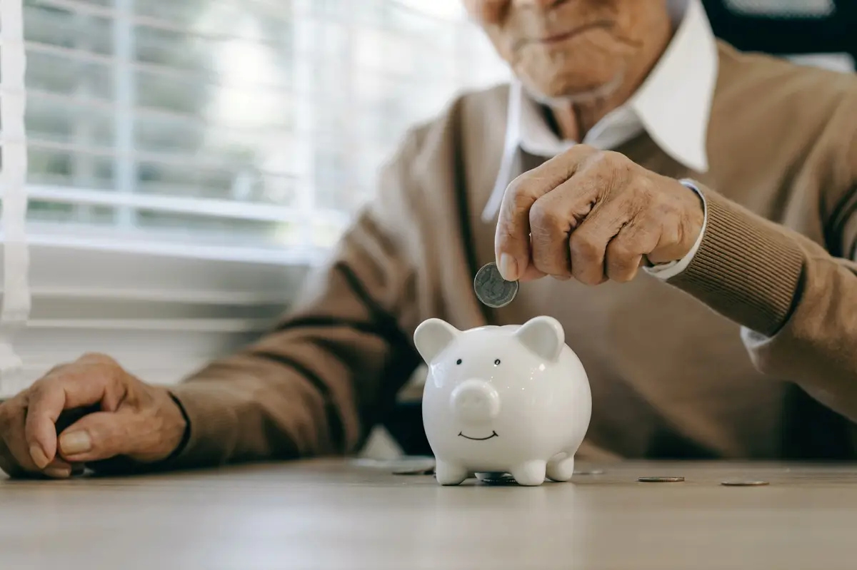 důchdci 3 - SportDeník Muž v seniorském věku vkládá minci do porcelánového prasátka
