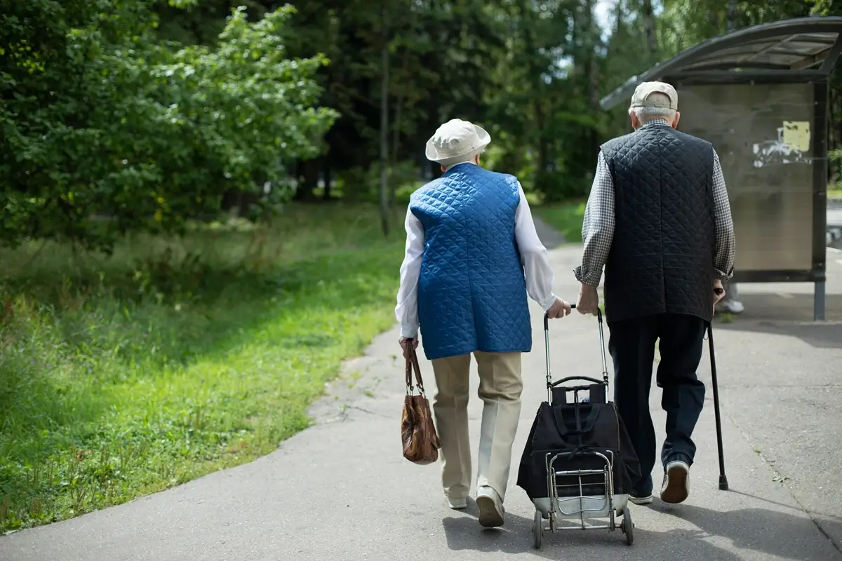 důchodci 1 - SportDeník Seniorský pár jde parkem a nákupní taškou na kolečkách