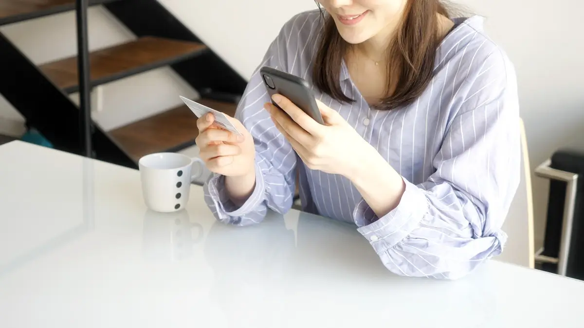 Mladá žena s mobilem v ruce, v druhé drží klasickou plastovou občanku