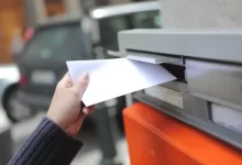 Ženská ruka vkládá dopis do klasické oranžové poštovní schránky