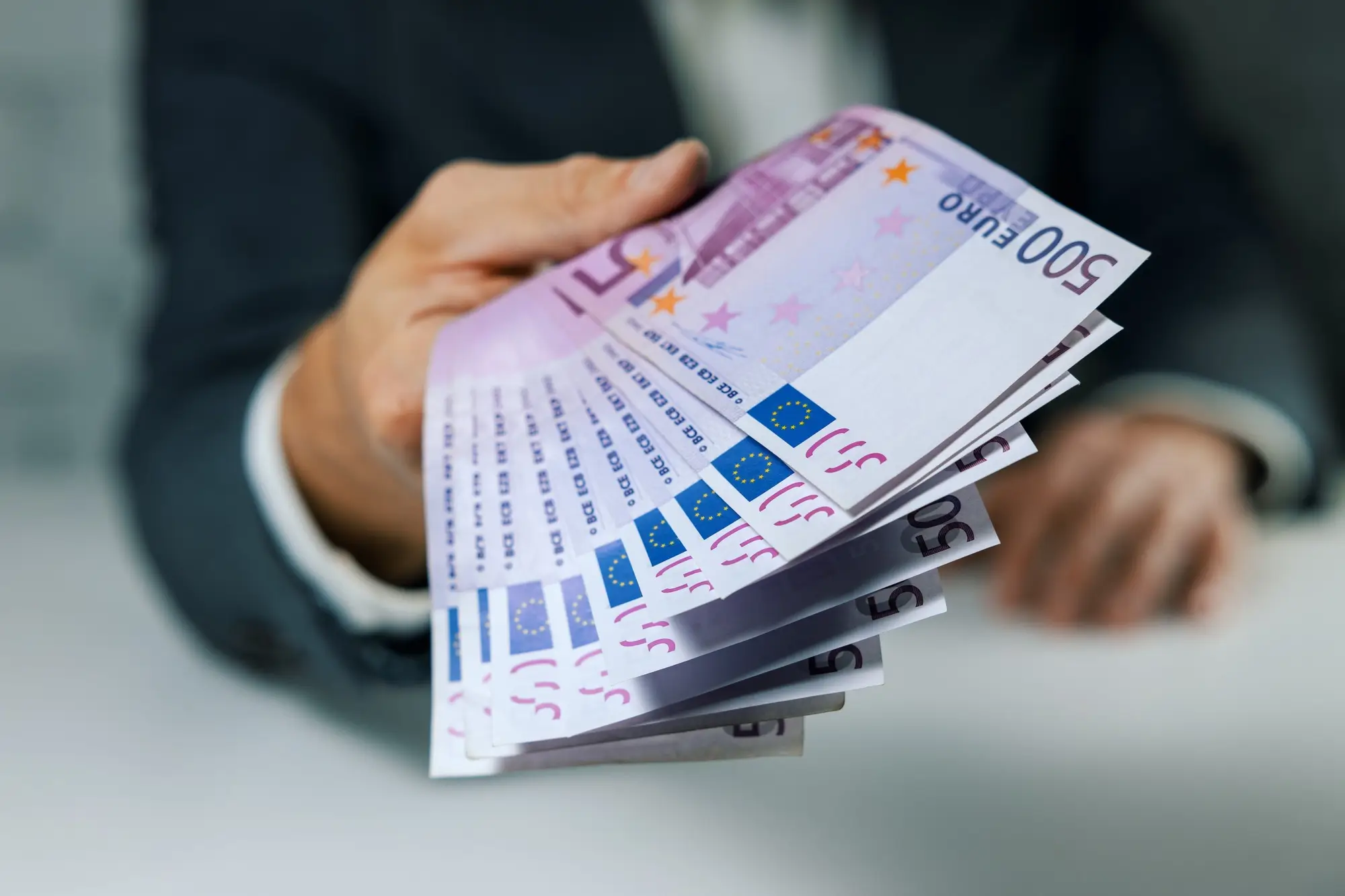 Muž podávající velký balík euro bankovek